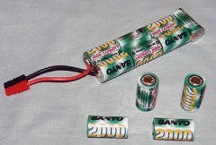 Battery and cells. At the top is a 7-cell battery (or pack) made up of seven Sanyo RC2000 cells. Four loose RC2000 cells are in the foreground. The battery was constructed by soldering two sticks of three cells end-to-end, and then soldering a seventh cell to the ends of the sticks using copper braid as a conductor. The whole pack is then enclosed in heat shrinkable plastic.