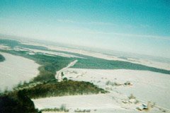 The view looking north-west, from about 800ft. The line that starts at the bottom right corner is the road we live on. It goes west, and then north-west to get around the lake (visible at the left side of the photo). The buildings at the bottom right corner are our neighbour's farm. Two more farms are visible on the other side of the road.